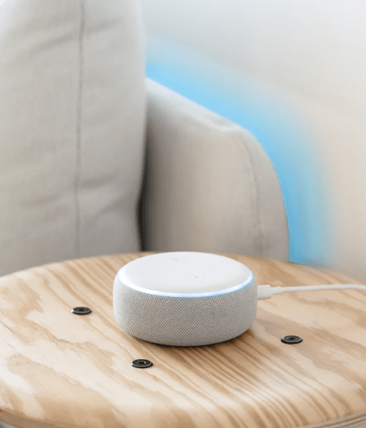 Wyze Light Strip lighting up the side of a couch and a voice assistant device placed on a table.