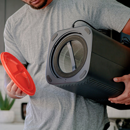 Man holding Wyze Air Purifier upside down with one arm and holding the bottom air filter cover with other hand, showing the air filter inside.