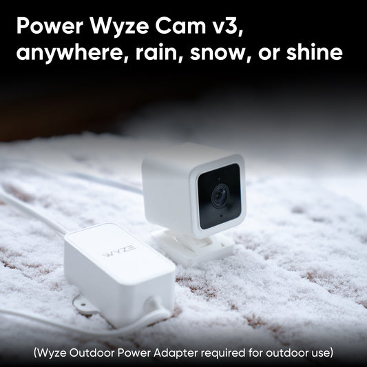 Wyze Cam v3 with an attached Wyze Outdoor Power Adapter sitting in snow. White text overlay that says "Wyze Outdoor Power Adapter required for outdoor use."